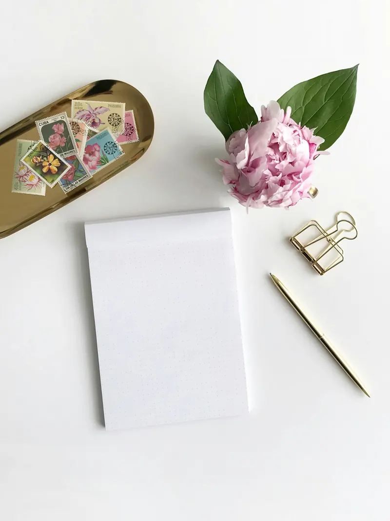Bloc-notes, stylo doré et pivoine posés sur un bureau blanc