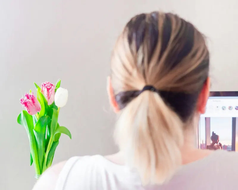 Femme de dos devant son écran, bouquet de tulipes sur le bureau